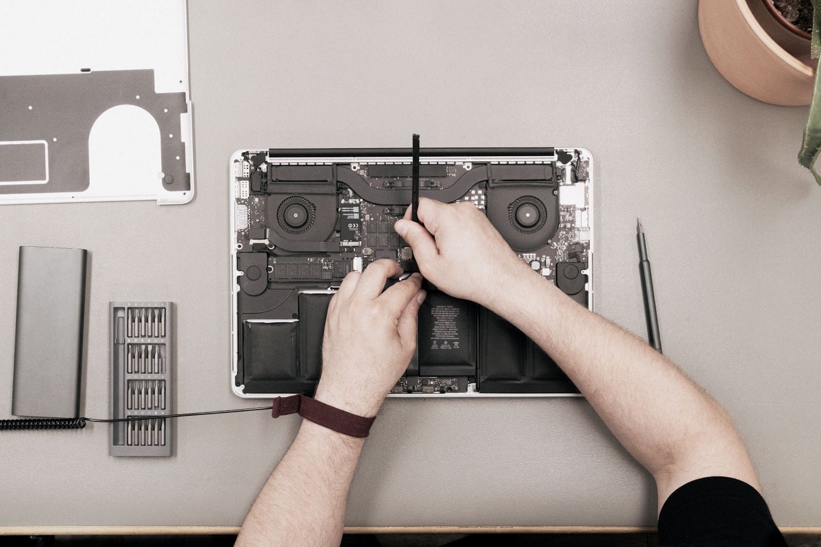 An opened MacBook Pro on a bench, its lower case removed, being worked on with a spudger.